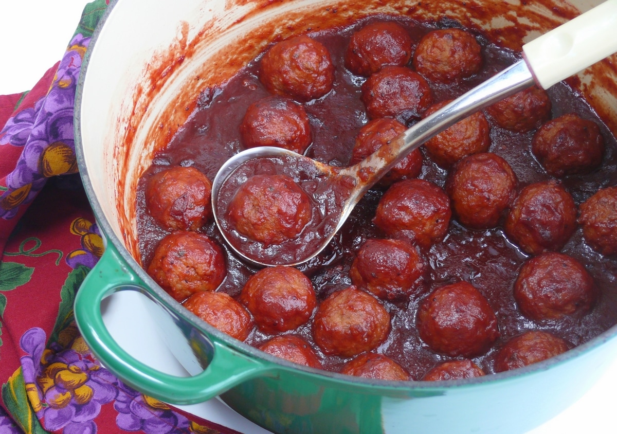 Kicked-Up Classic Cocktail Meatballs cooking in a Dutch oven with a flavorful, spicy sauce. Dutch oven filled with Kicked-Up Classic Cocktail Meatballs simmering in a rich, spicy sauce.