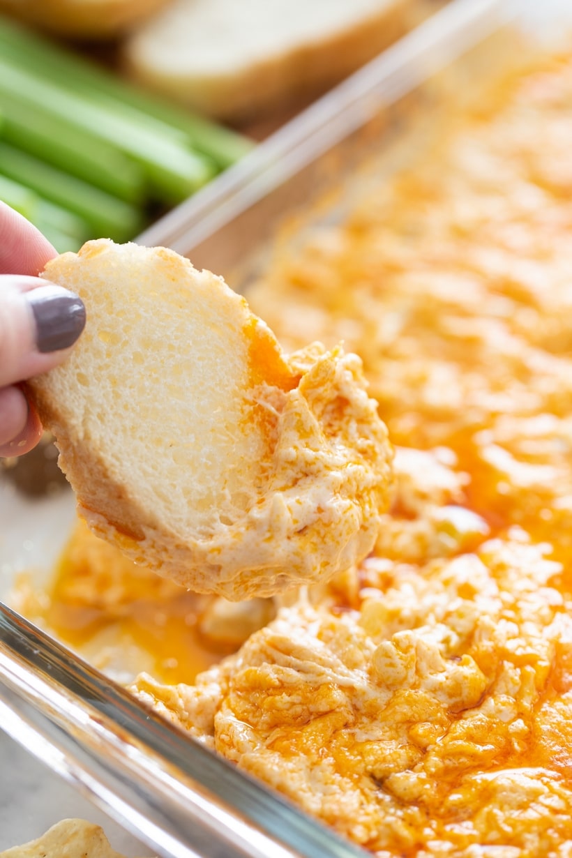 Hand dipping a baguette slice into creamy Buffalo chicken dip.