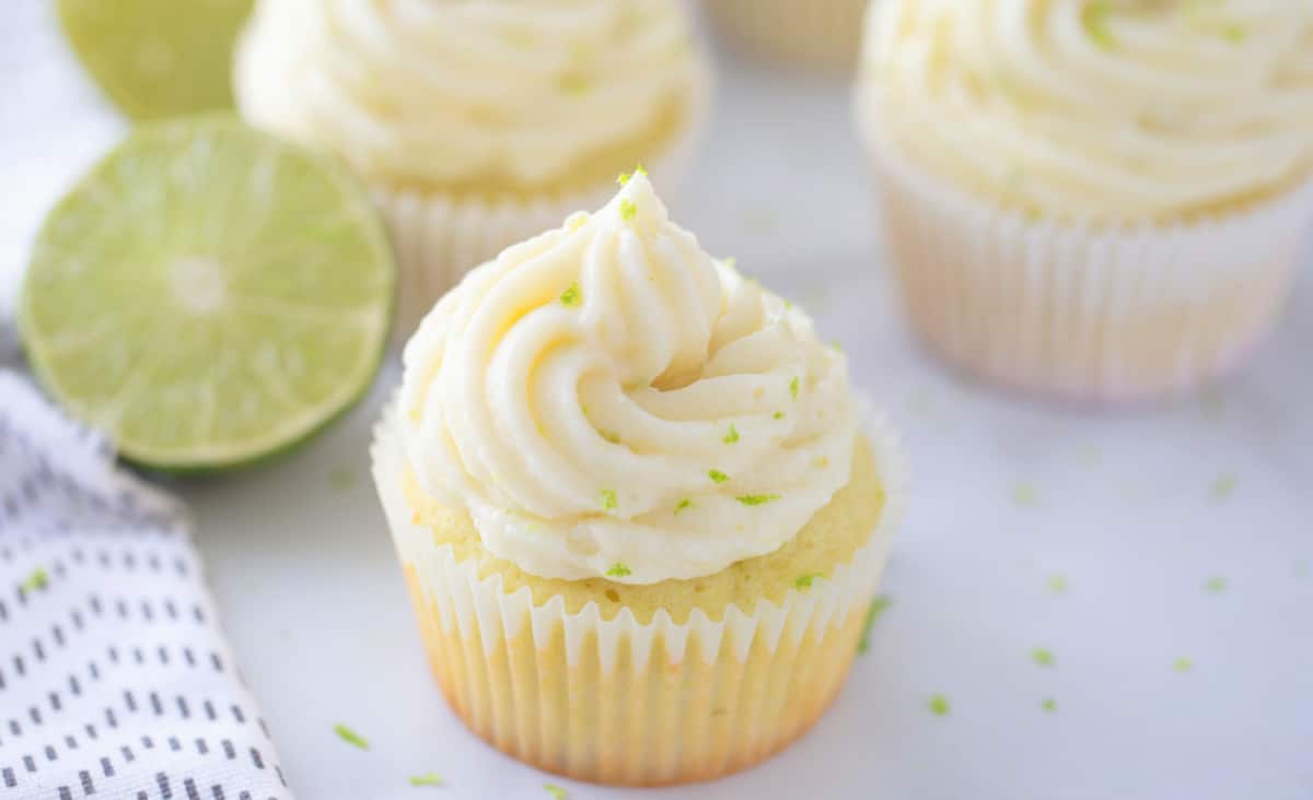 Three finished key lime cupcakes on a plate, topped with cream cheese frosting and lime zest