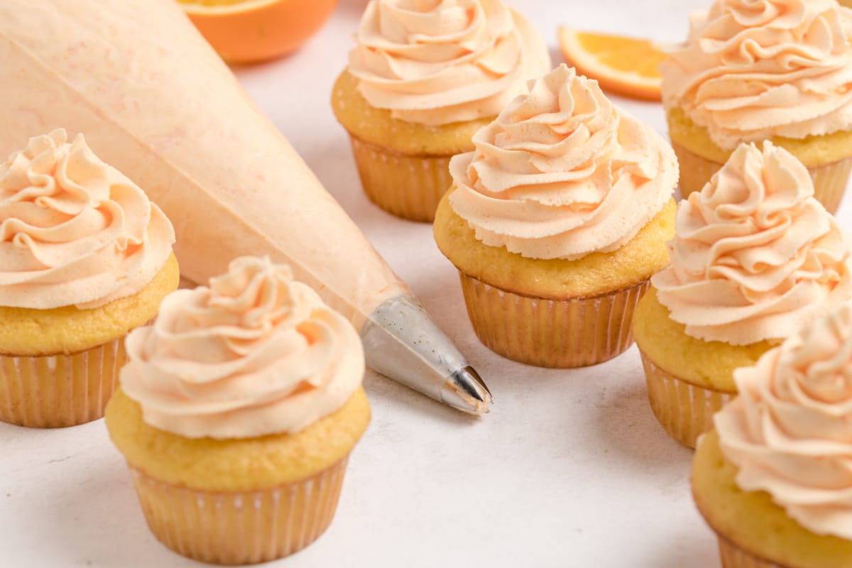 Orange Cupcakes with Whipped Orange Frosting with a piping bag Frosted orange cupcakes with a piping bag filled with whipped orange frosting, ready to add the finishing touches.
