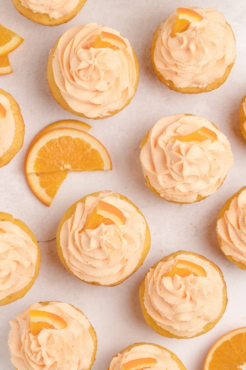 overhead of many Dreamy Orange Cupcakes with Whipped Orange Frosting A top-down view of frosted orange cupcakes garnished with orange slices, highlighting their bright color and fluffy texture.