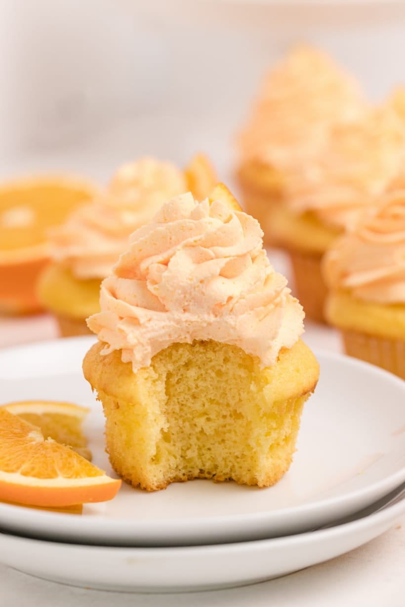 Dreamy Orange Cupcakes with Whipped Orange Frosting with a bite taken A single Dreamy Orange Cupcake on a plate with a bite taken out, showing its soft texture and creamy whipped orange frosting.