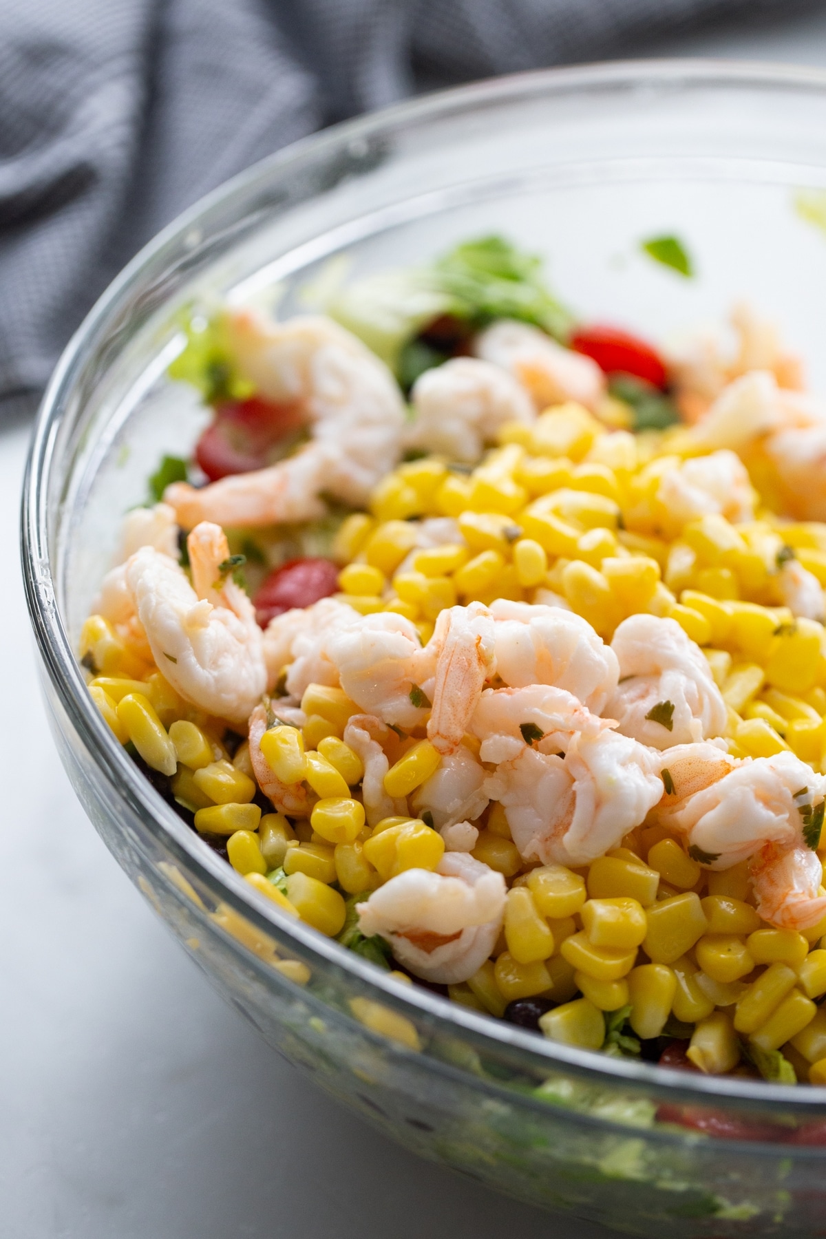 Shrimp and Avocado Taco Salad in a clear bowl mixing the corn and shrimp into the shrimp and avocado taco salad