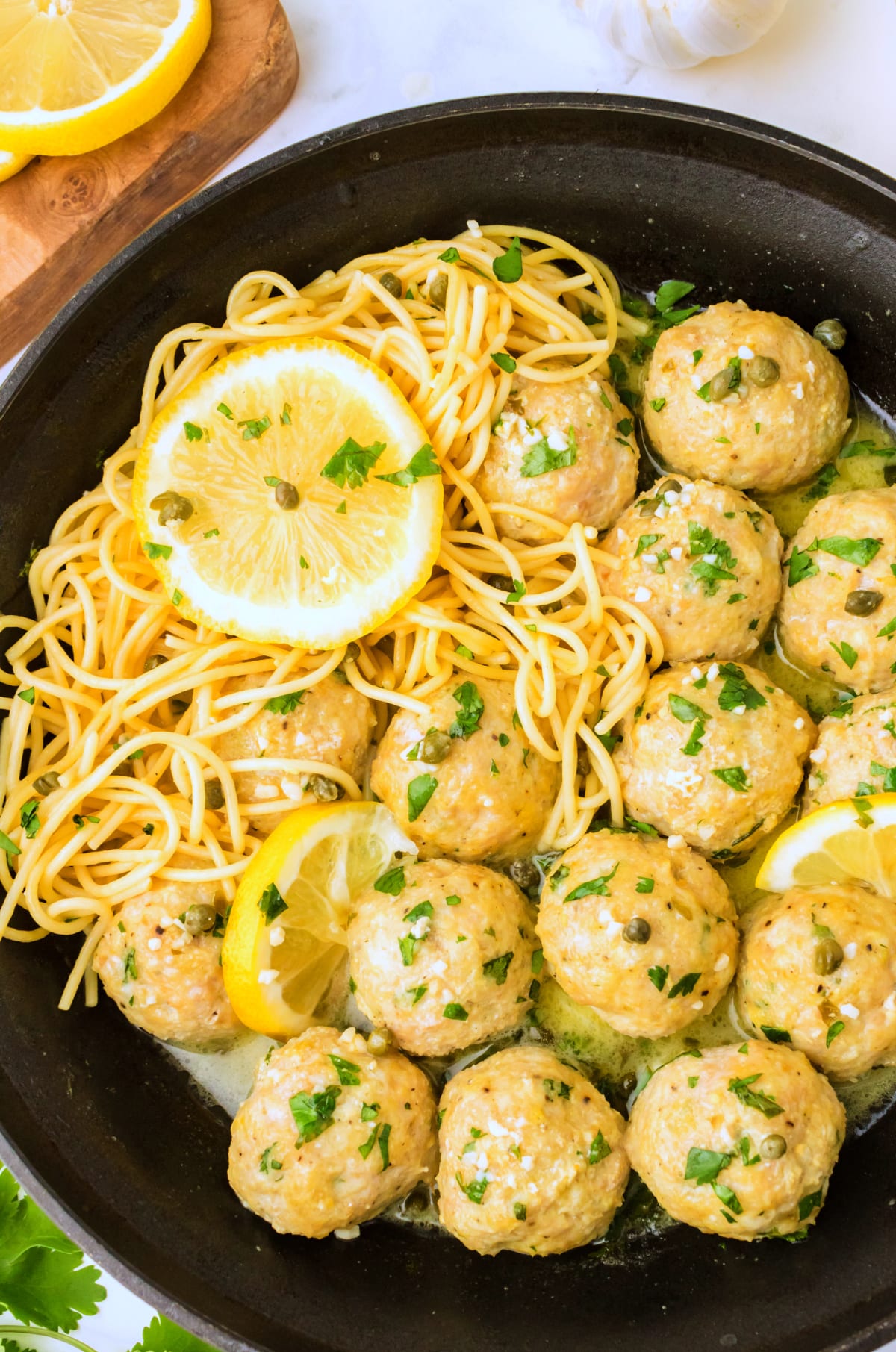 skillet of chicken piccata meatballs with lemon and capers Chicken piccata meatballs in skillet with sliced lemon and capers, overhead view