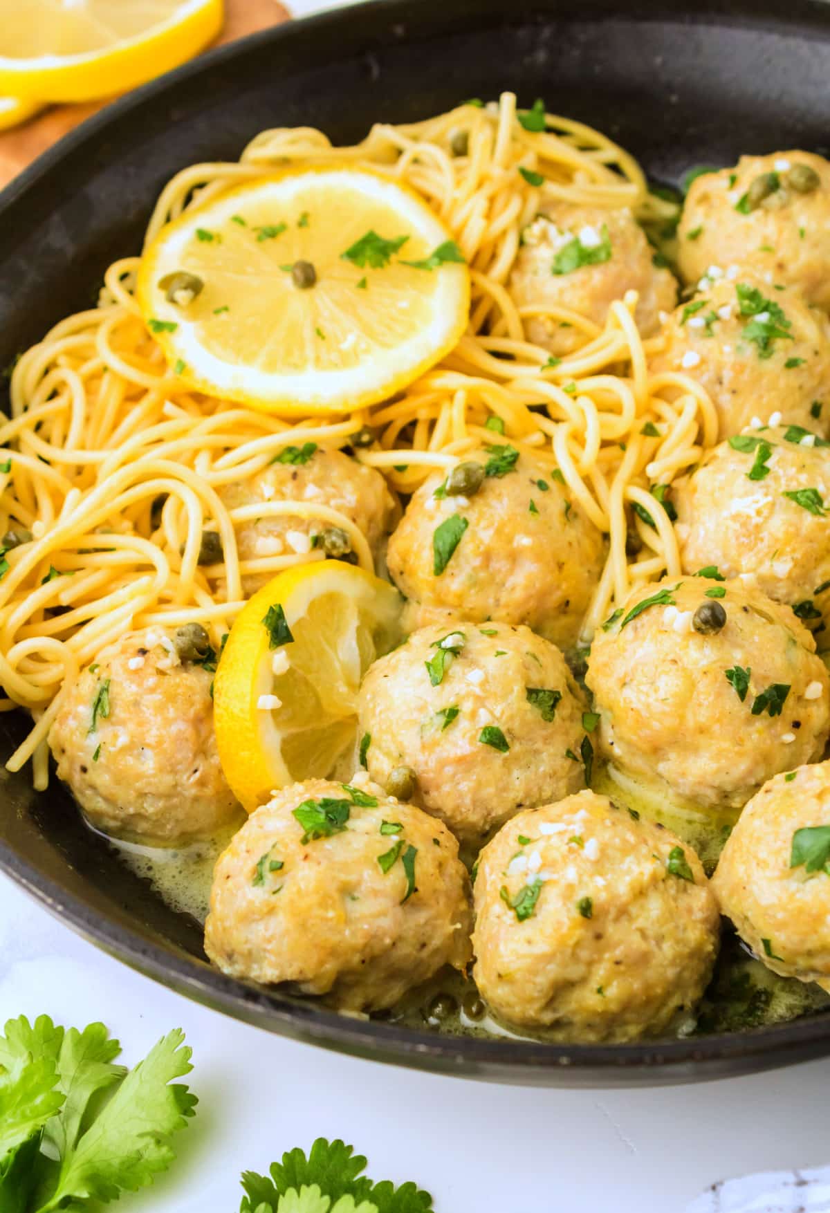 chicken piccata meatballs in skillet with pasta and lemon Baked chicken piccata meatballs in a skillet with pasta and lemon slices, side view