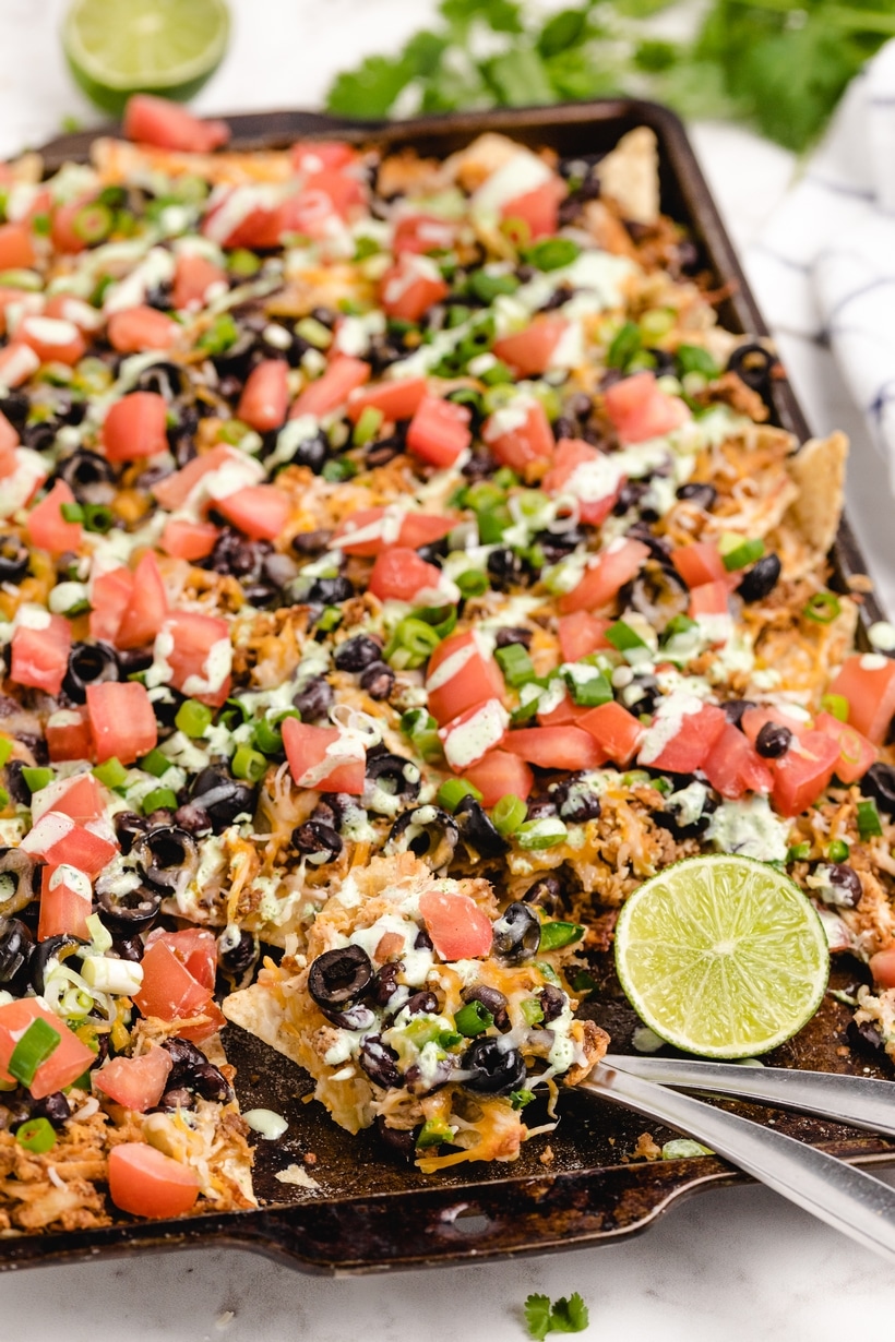 It's time to add these sheet pan chicken nachos with a creamy lime drizzle to your weekly meal plan. These loaded nachos are quick, flavorful, easily customizable, and budget-friendly. I make them whenever I have leftover rotisserie chicken. rotisserie chicken nachos