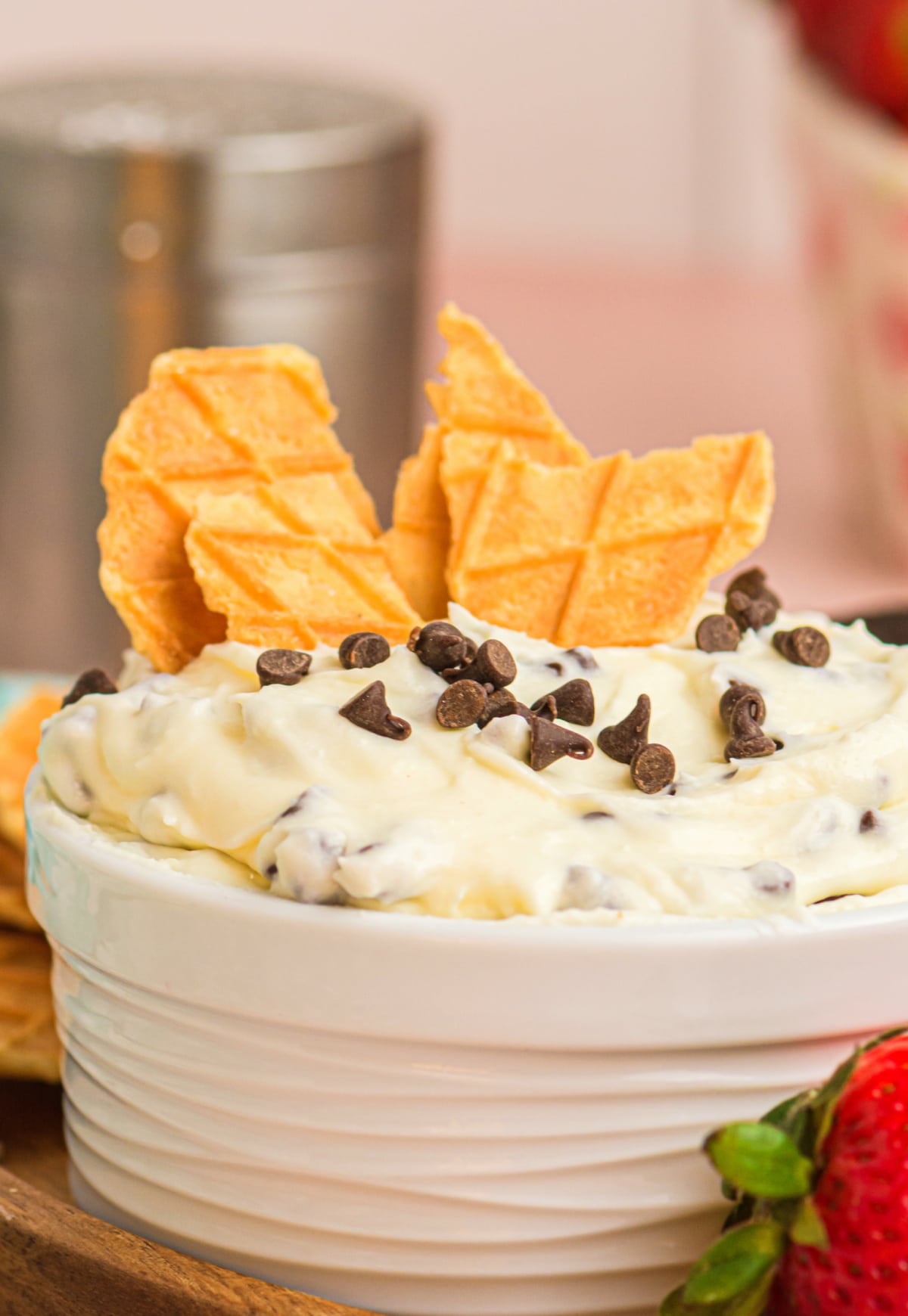 Cannoli dip with waffle cone and chocolate chips Cannoli dip in a white serving ramekin topped with mini chocolate chips and waffle cone pieces sticking out