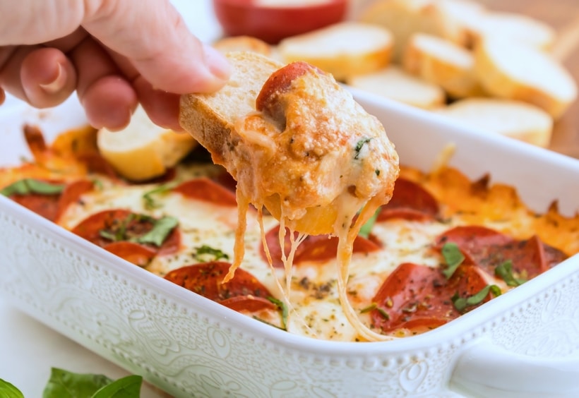 Scooped pizza dip with a dipper of bread. pizza dip taking out a scoop