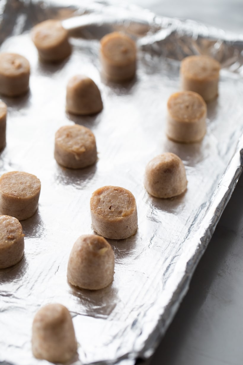 Unbaked sausage bites arranged on a tray, prepped for cooking. Sliced chicken sausage pieces arranged on a rimmed baking tray, ready to bake.