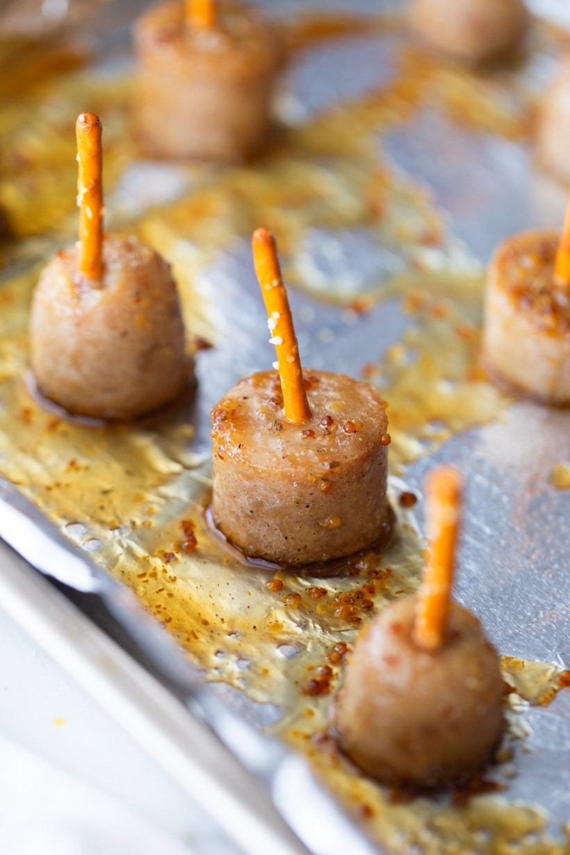 Finished maple-glazed sausage bites on a baking tray with pretzel skewers. Maple-glazed sausage bites skewered with pretzel sticks on a baking tray, ready to serve.
