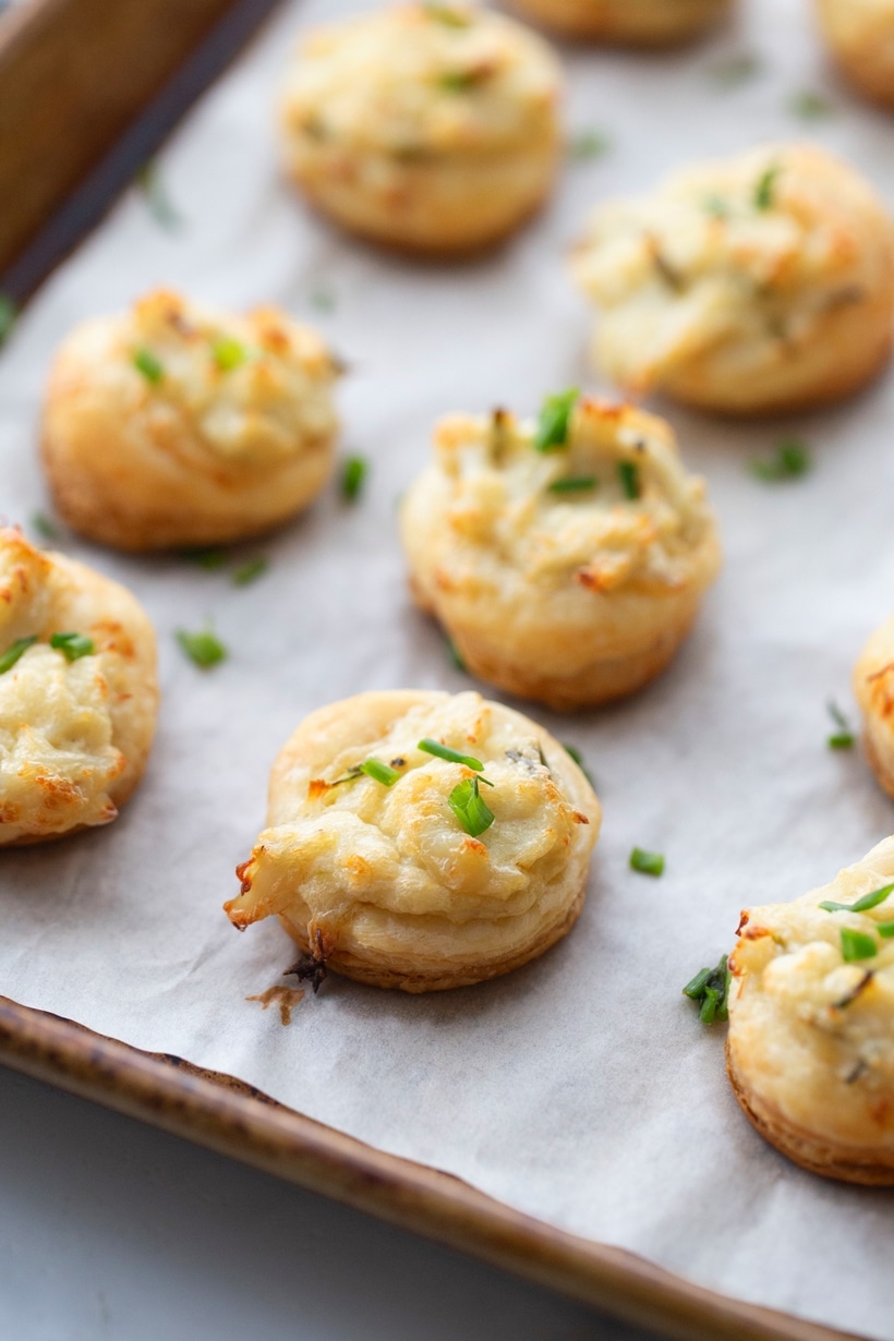 Golden brown crab and chive puffs freshly baked on a parchment-lined baking sheet.