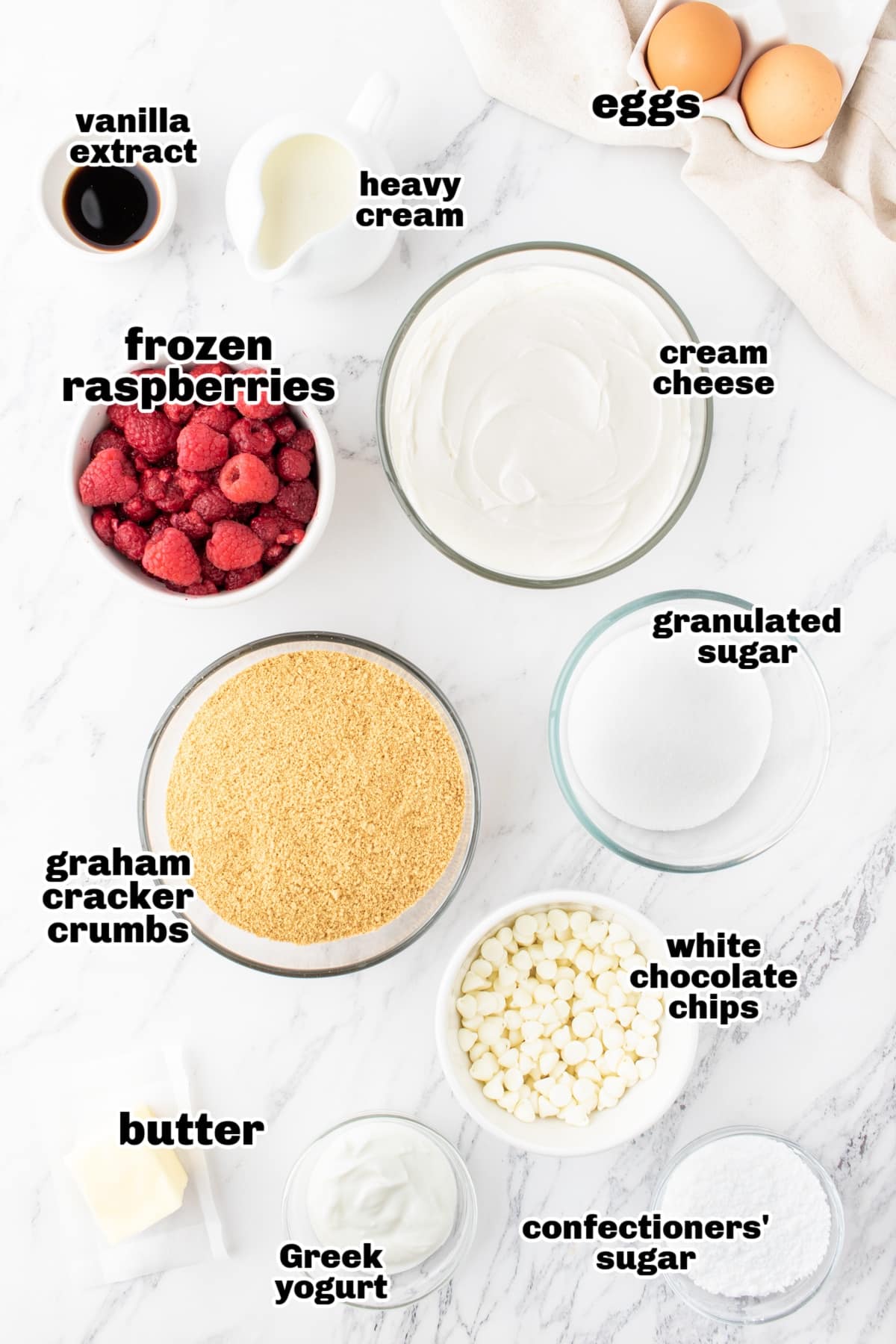 Ingredients for mini white chocolate raspberry cheesecakes, including graham crackers, raspberries, cream cheese, and white chocolate.
