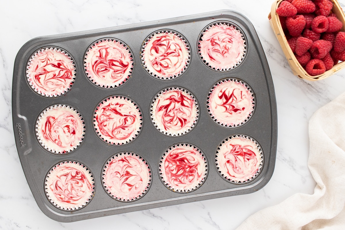 Overhead view of a muffin tin filled with baked mini white chocolate raspberry swirl cheesecakes.