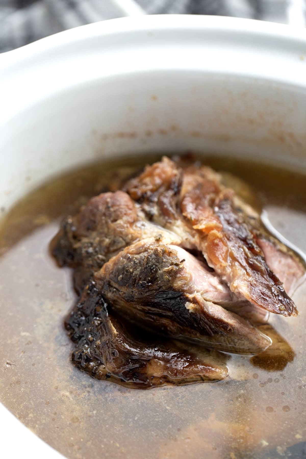 Whole pork butt sitting in seasoned liquid inside the slow cooker