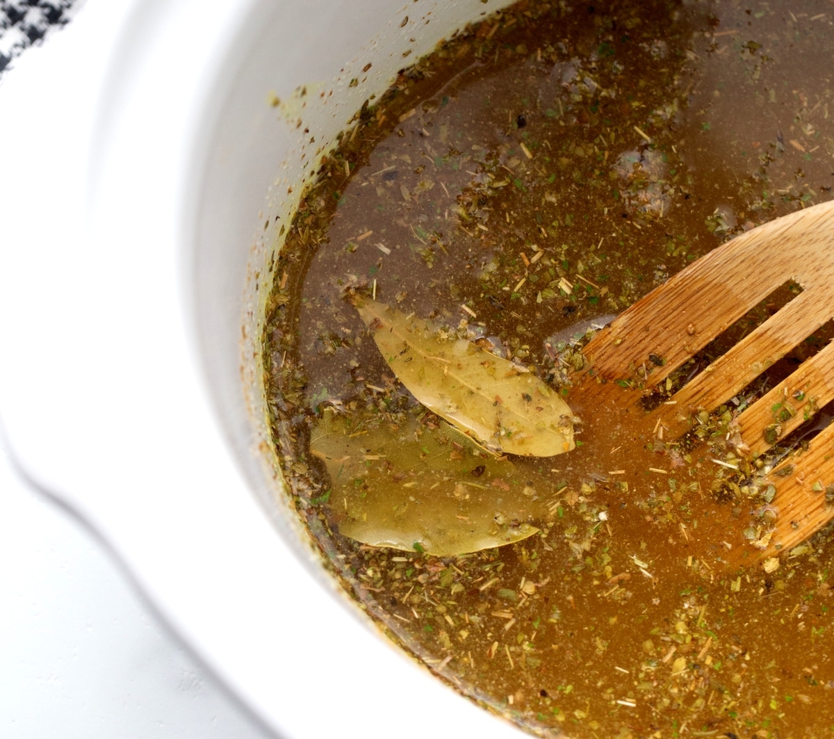 Overhead view of slow cooker filled with liquid, spices, and bay leaves before cooking