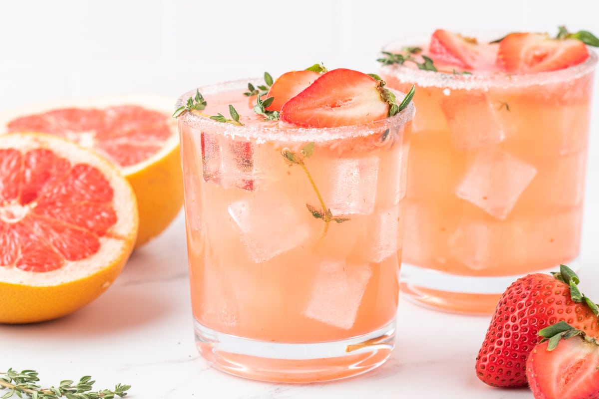 Two Strawberry Grapefruit Palomas Side view of two palomas with sliced grapefruit and strawberries arranged around the glasses.