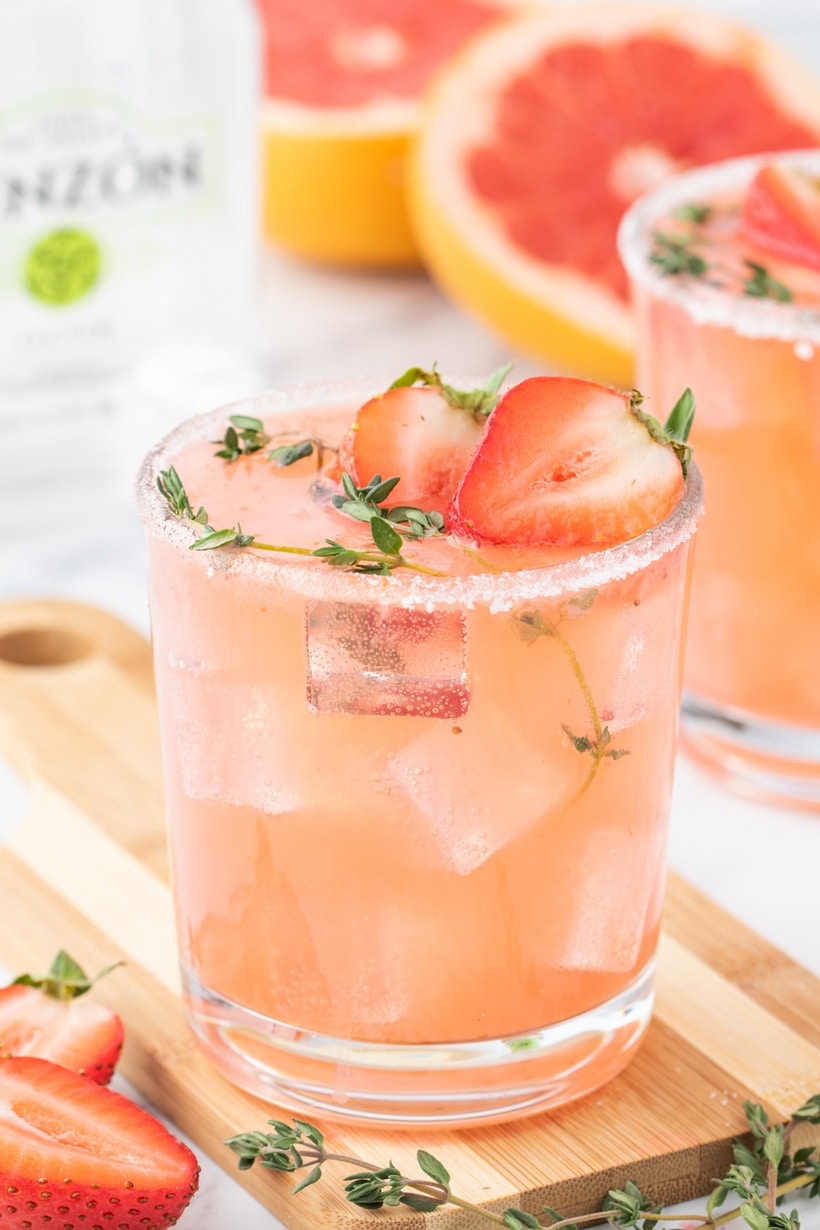 Strawberry Grapefruit Paloma on a cutting board Single paloma on a cutting board with sliced grapefruit and a bottle of tequila in the background.
