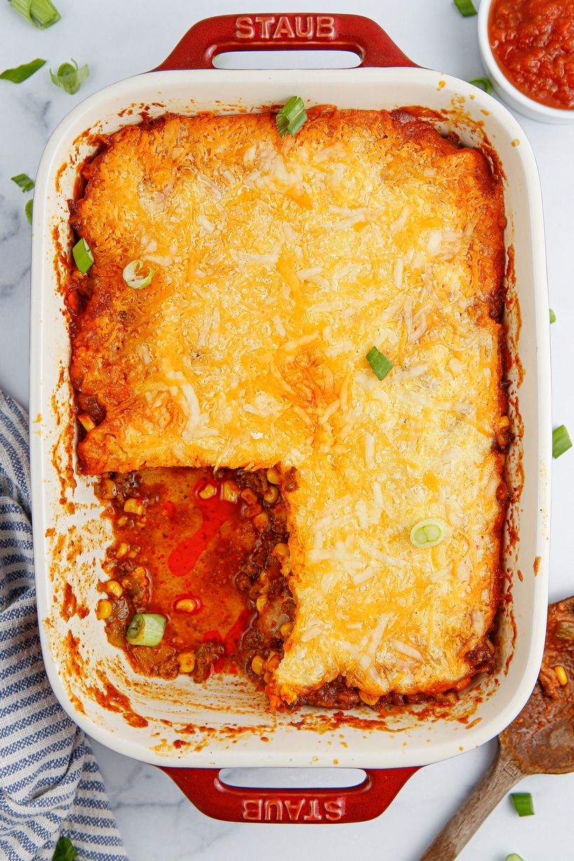 Tamale pie in a baking dish with a serving taken out, showing the cornbread topping and savory beef filling.