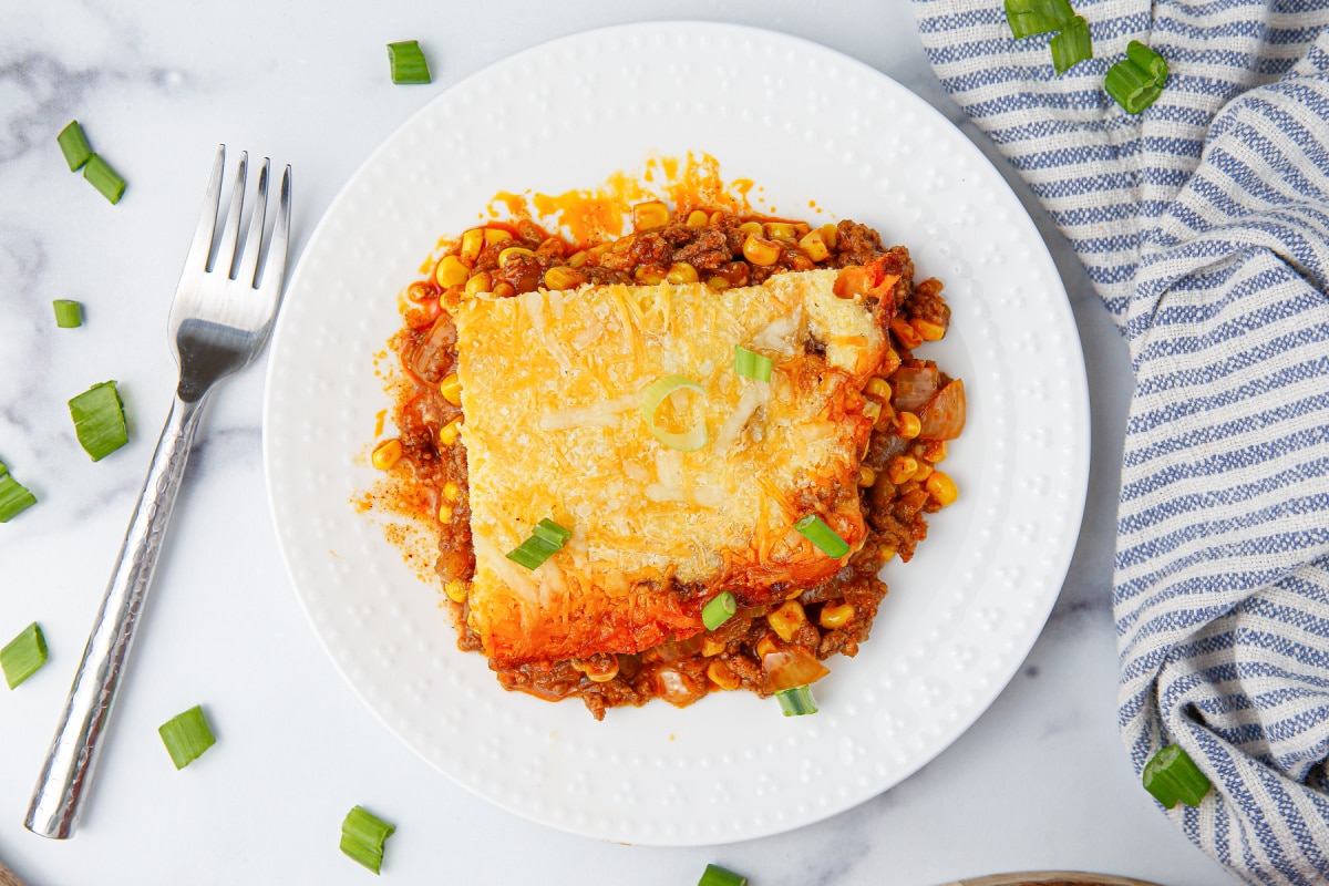 A plated serving of tamale pie on a white plate, showing the golden cornbread crust and cheesy beef filling.