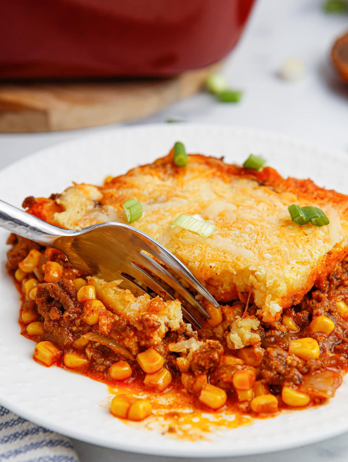 A single serving of tamale pie on a plate with the full casserole dish blurred in the background.