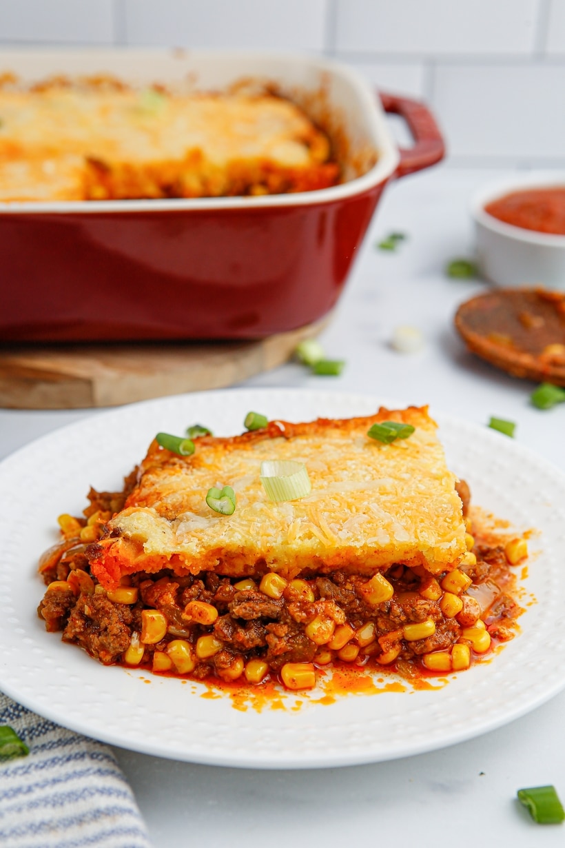A single serving of tamale pie on a plate with the full casserole dish blurred in the background.