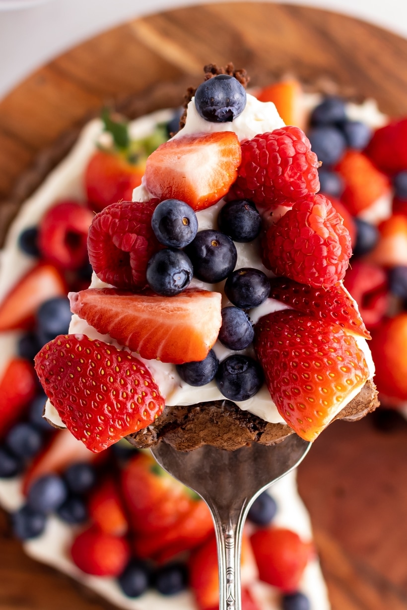 brownie dessert pizza slice with strawberries, raspberries, and blueberries Slice of brownie dessert pizza with fresh fruit and frosting