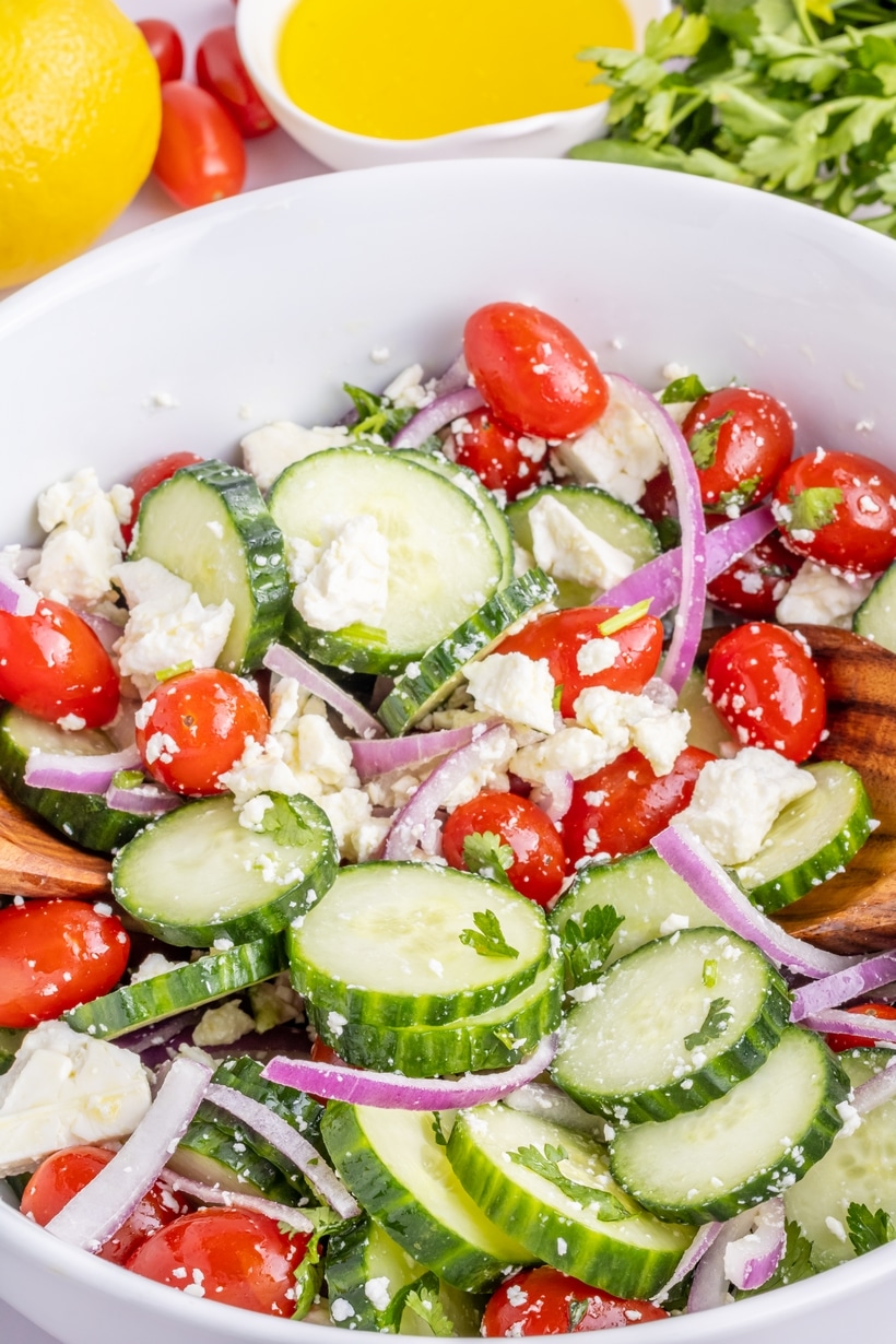 Feta Cucumber Salad with Tomatoes and Fresh Parsley Close-up of sliced cucumber, grape tomatoes, feta, and red onion mixed with herbs and lemon vinaigrette.