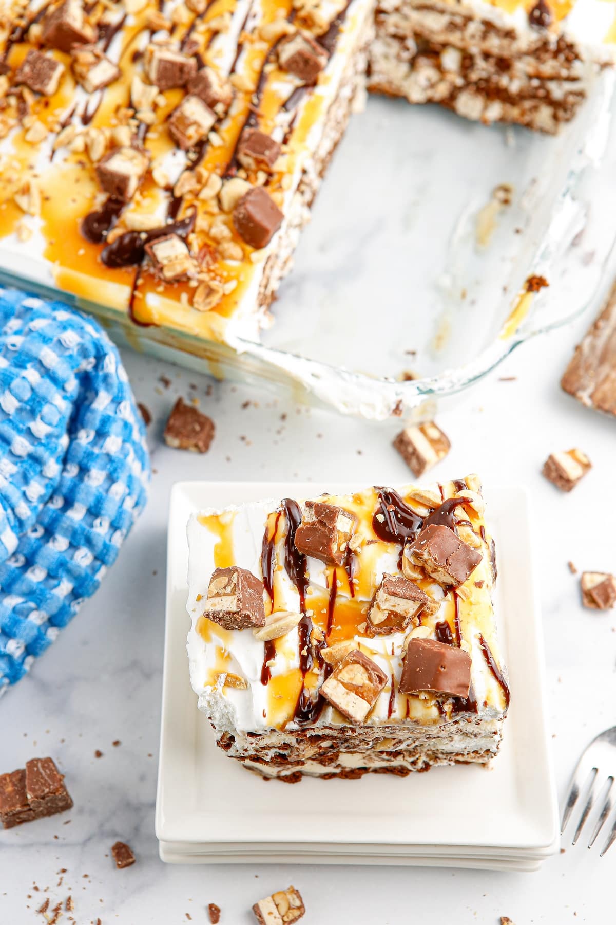 Snickers ice cream casserole topped with caramel, chocolate sauce, chopped peanuts, and Snickers bars