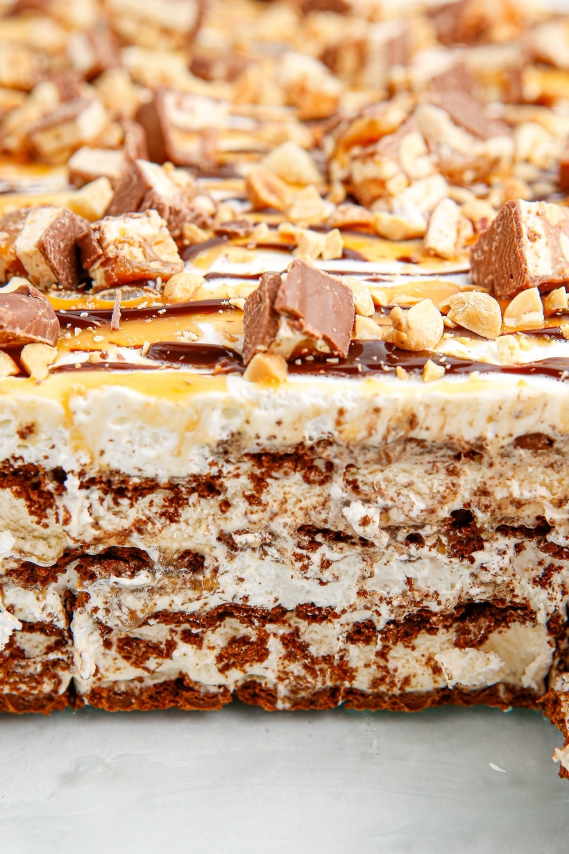 Close-up of layered snickers ice cream sandwich cake with chopped candy bars, peanuts, caramel, and chocolate drizzle