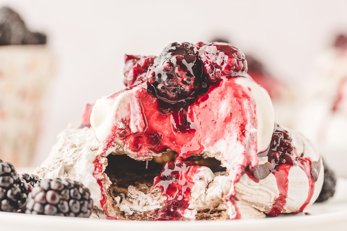 Broken chocolate blackberry pavlova showing the soft center beneath whipped cream, blackberry compote and fresh blackberries.