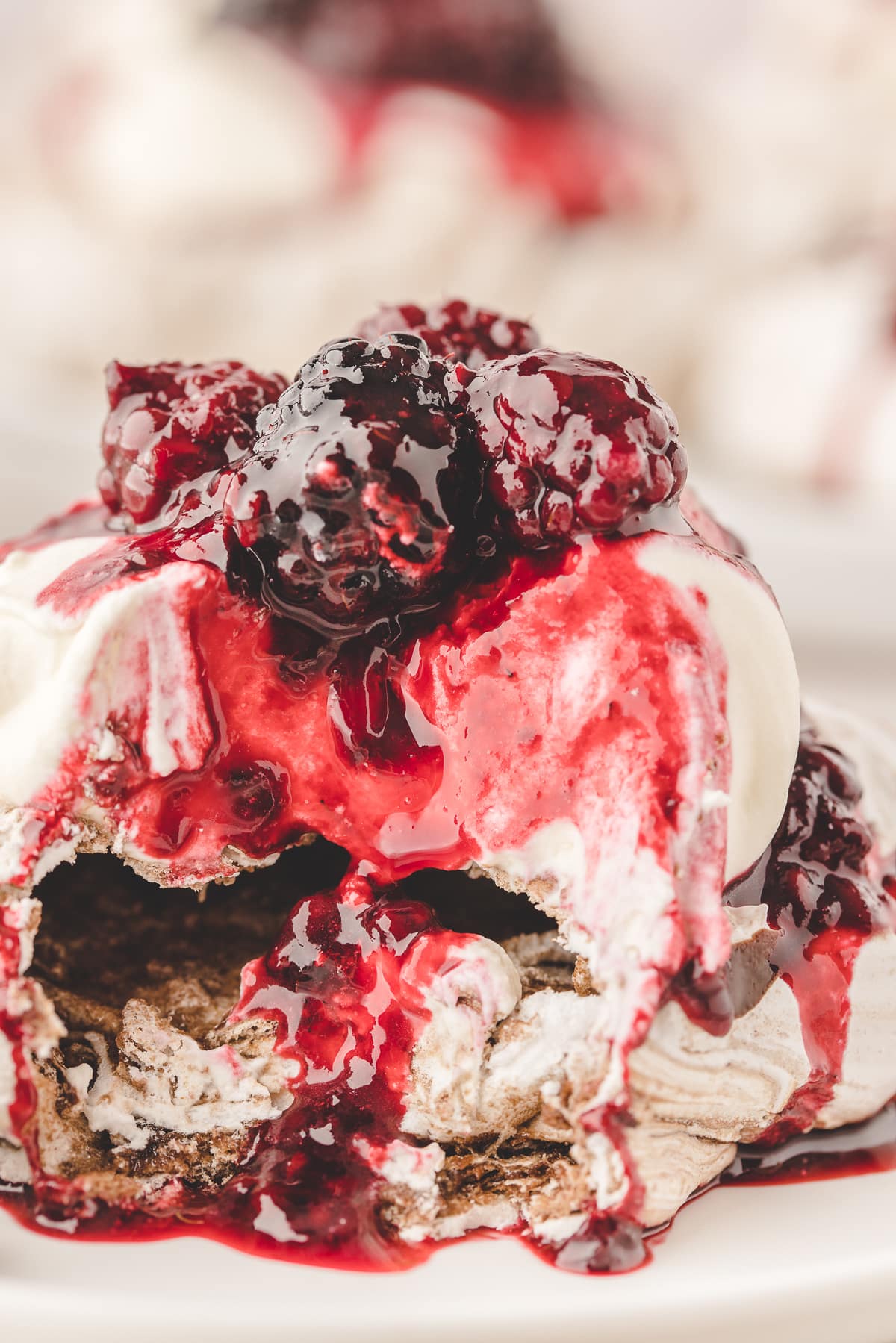 Broken chocolate-swirled pavlova showing its soft center beneath whipped cream, blackberry compote and whole blackberries.