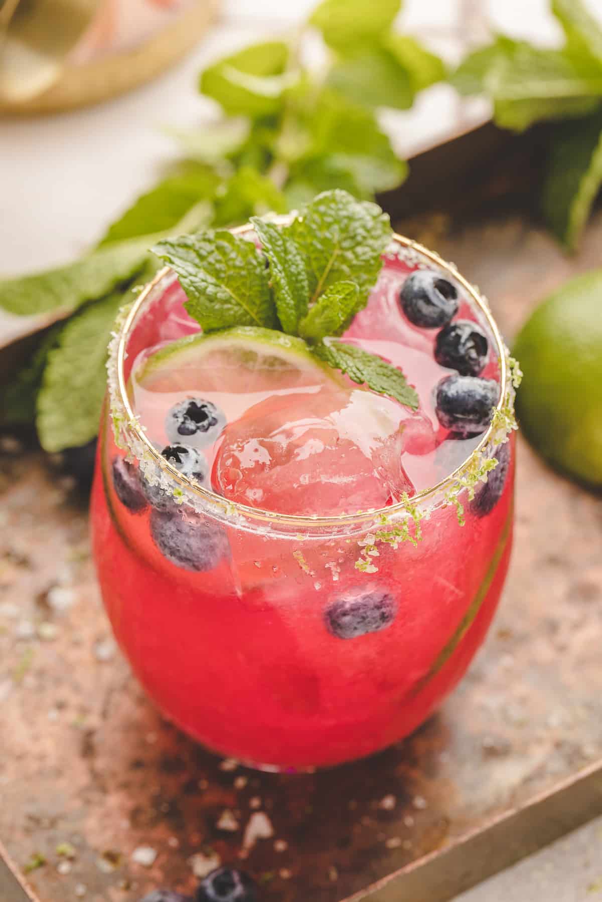 Blueberry Margarita in a glass A vibrant blueberry margarita served on the rocks with a lime salt rim, fresh blueberries, and a mint sprig.
