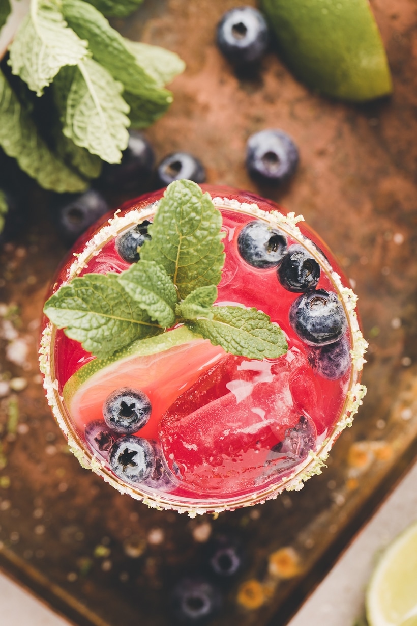 A poured Blueberry margarita Blueberry margarita mix being poured from a shaker through a strainer into a glass filled with ice.