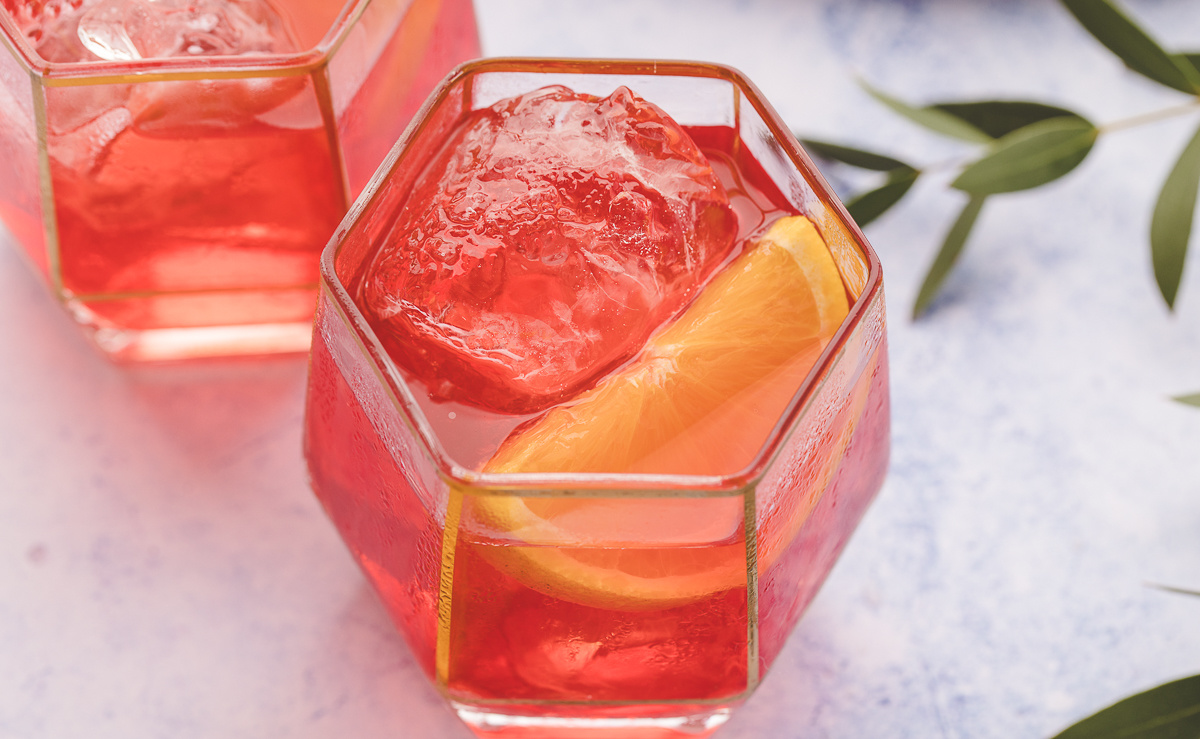 Two Negronis with ice and orange wedge garnish Two Negroni cocktails on the rocks, each served with an orange wedge garnish.