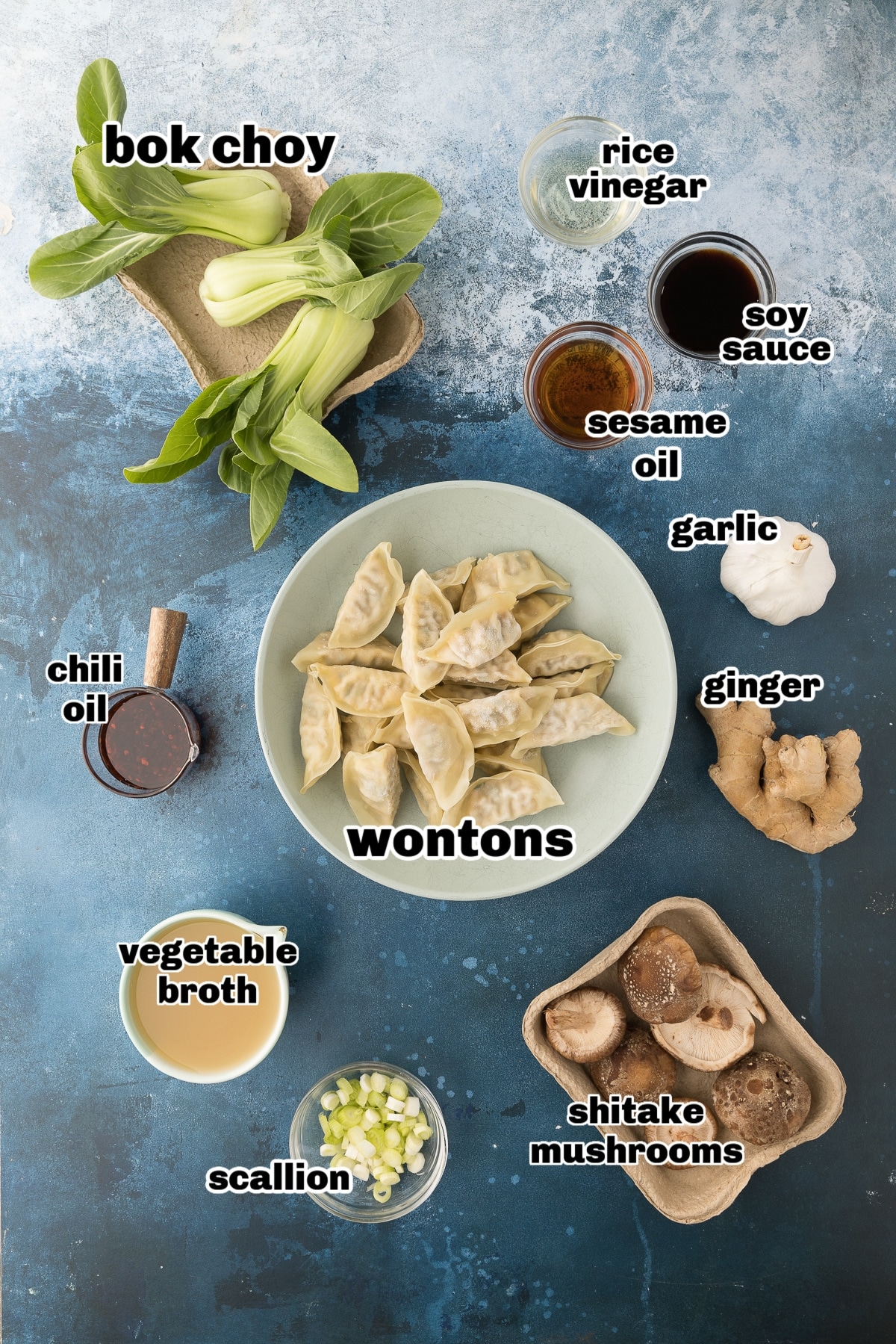 Ingredients for Easy 20-Minute Wonton Soup Ingredients for wonton soup arranged on a countertop, including sesame oil, bok choy, garlic, ginger, mushrooms, broth, frozen wontons, rice vinegar, soy sauce, scallions, sesame seeds, and chili oil.