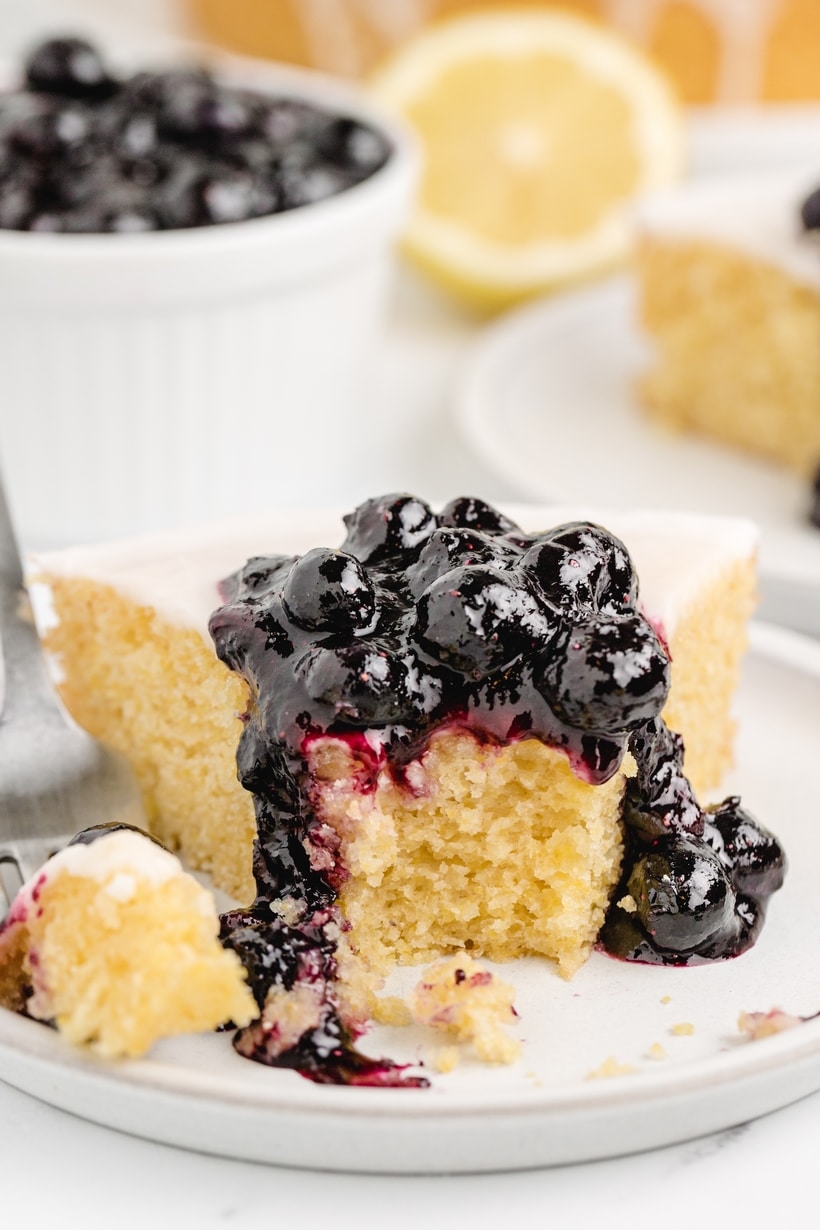 Lemon Cornmeal Cake bite removed A slice of lemon cornmeal cake topped with blueberry sauce, with a bite removed to show the texture.