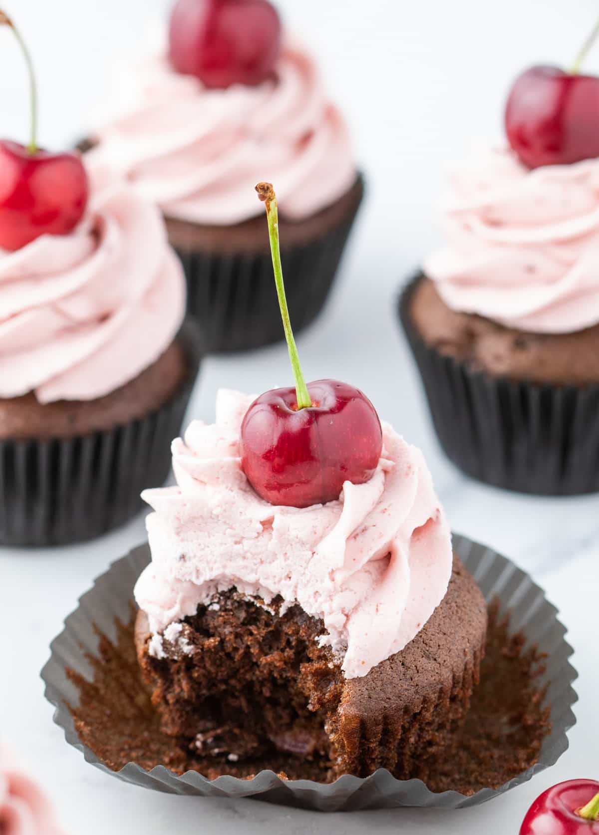 Chocolate cherry cupcake with a bite taken out, showing the moist texture and pieces of cherry inside.