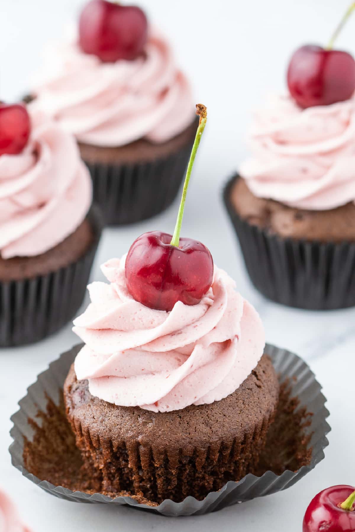 Chocolate cherry cupcake with the liner pulled down, showing the baked cherry-filled crumb.