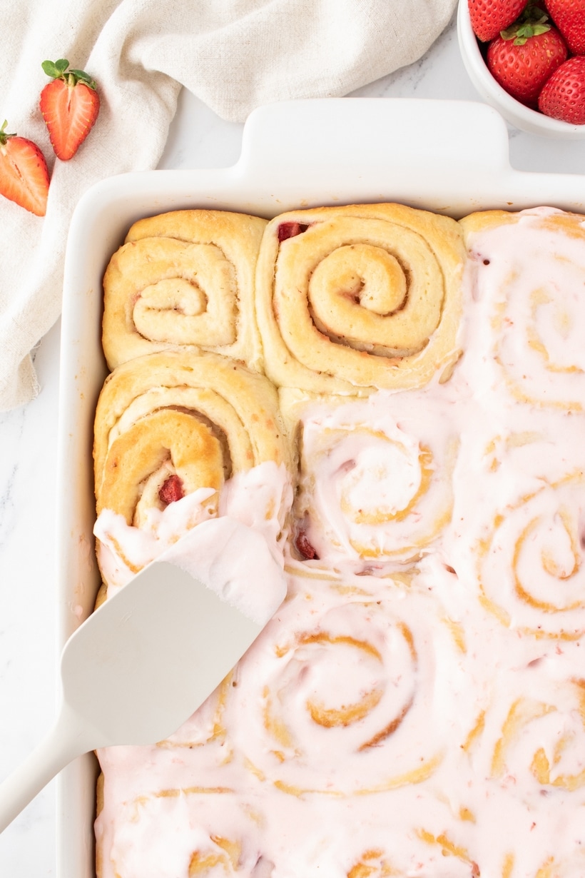 Strawberry Sweet Rolls being frosted Side view of a pan of strawberry sweet rolls halfway glazed, showing contrast between frosted and unfrosted.