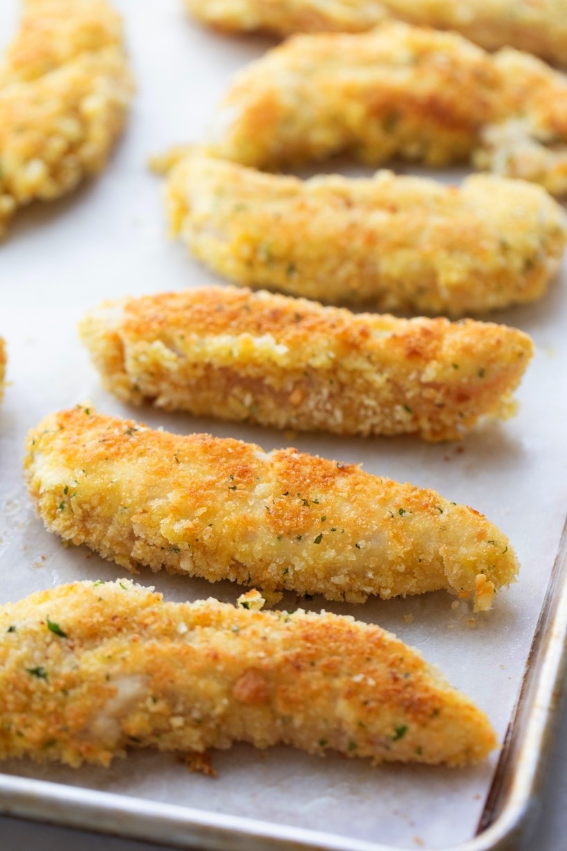 Chicken Tenderloin Piccata just out of the oven Crispy baked chicken tenderloins resting on a parchment-lined baking sheet after coming out of the oven.