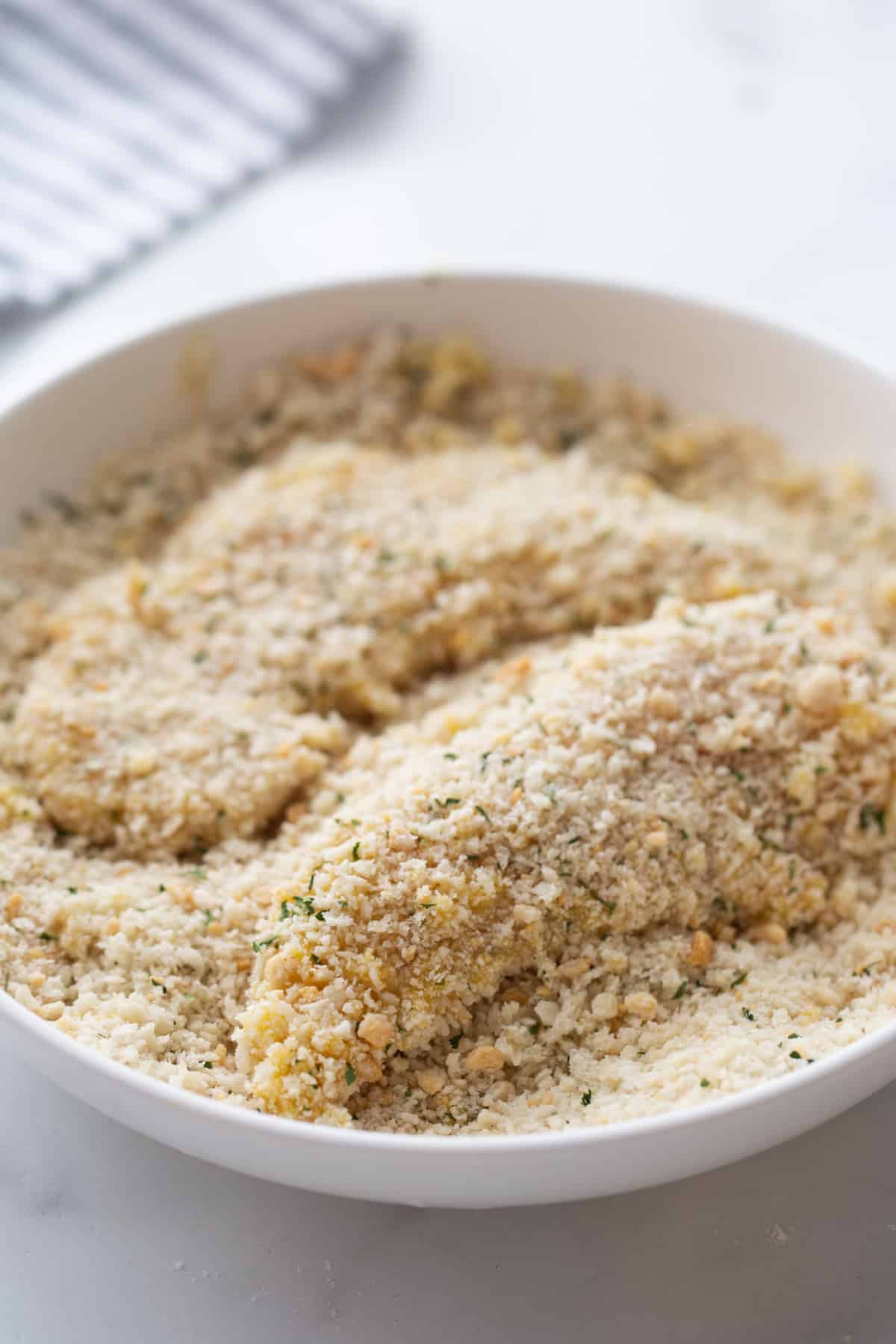 Chicken Tenderloin Piccata dredged in panko breadcrumbs A chicken tenderloin covered in egg being dipped into a bowl of panko breadcrumbs, ensuring a crispy coating.