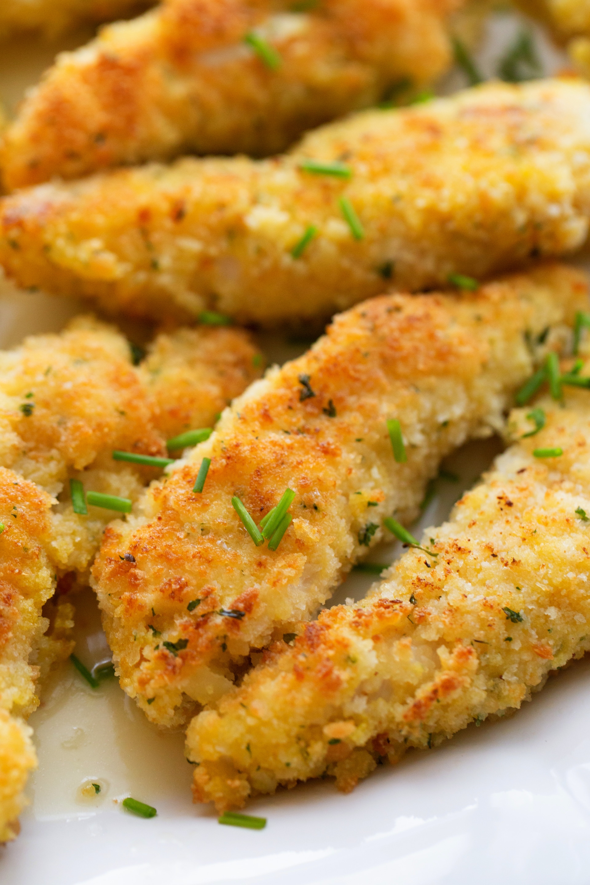 Chicken Tenderloin Piccata ready to eat A detailed view of crispy, golden chicken tenderloin piccata with a glistening lemon-butter sauce and fresh chives.