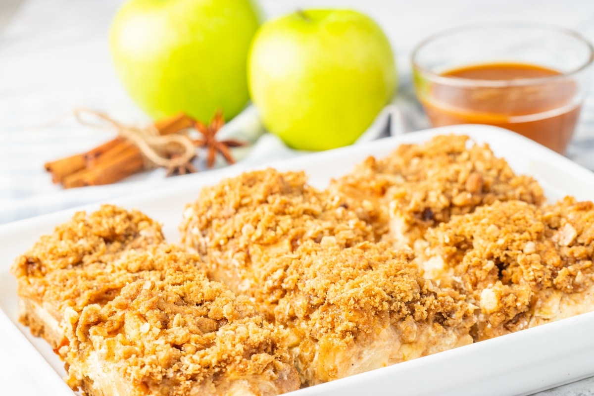Apple cheesecake bars with streusel topping lined up in a white baking dish.