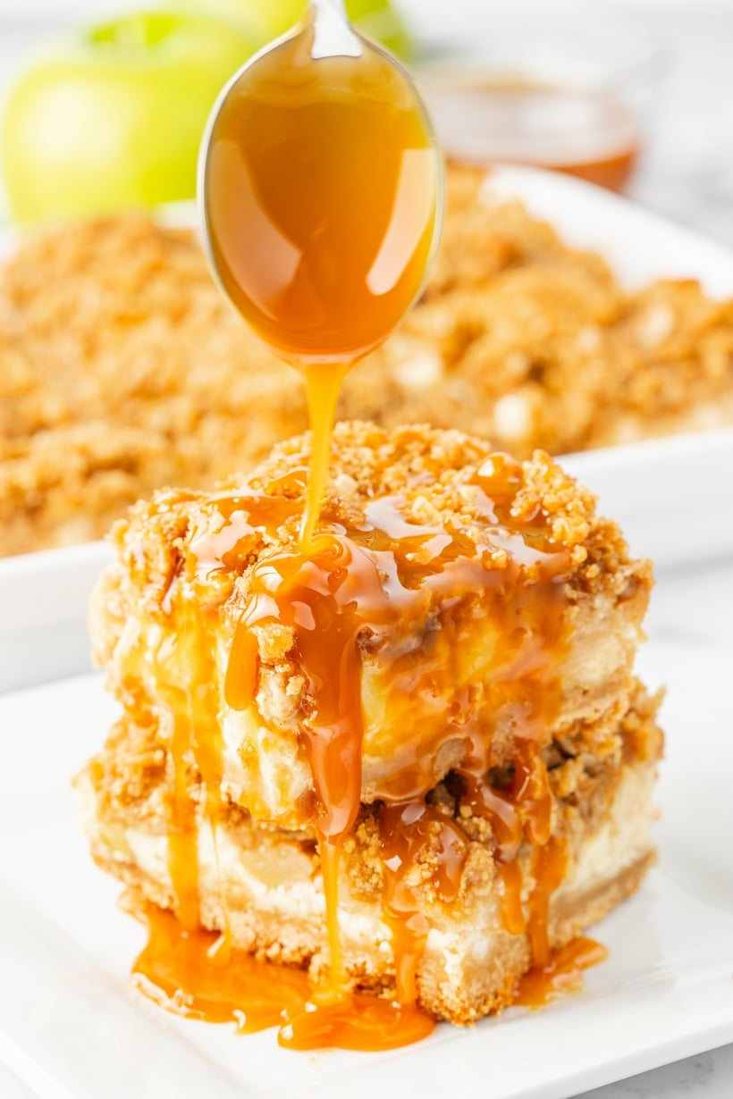 Caramel apple cheesecake bars stacked and drizzled with caramel sauce.