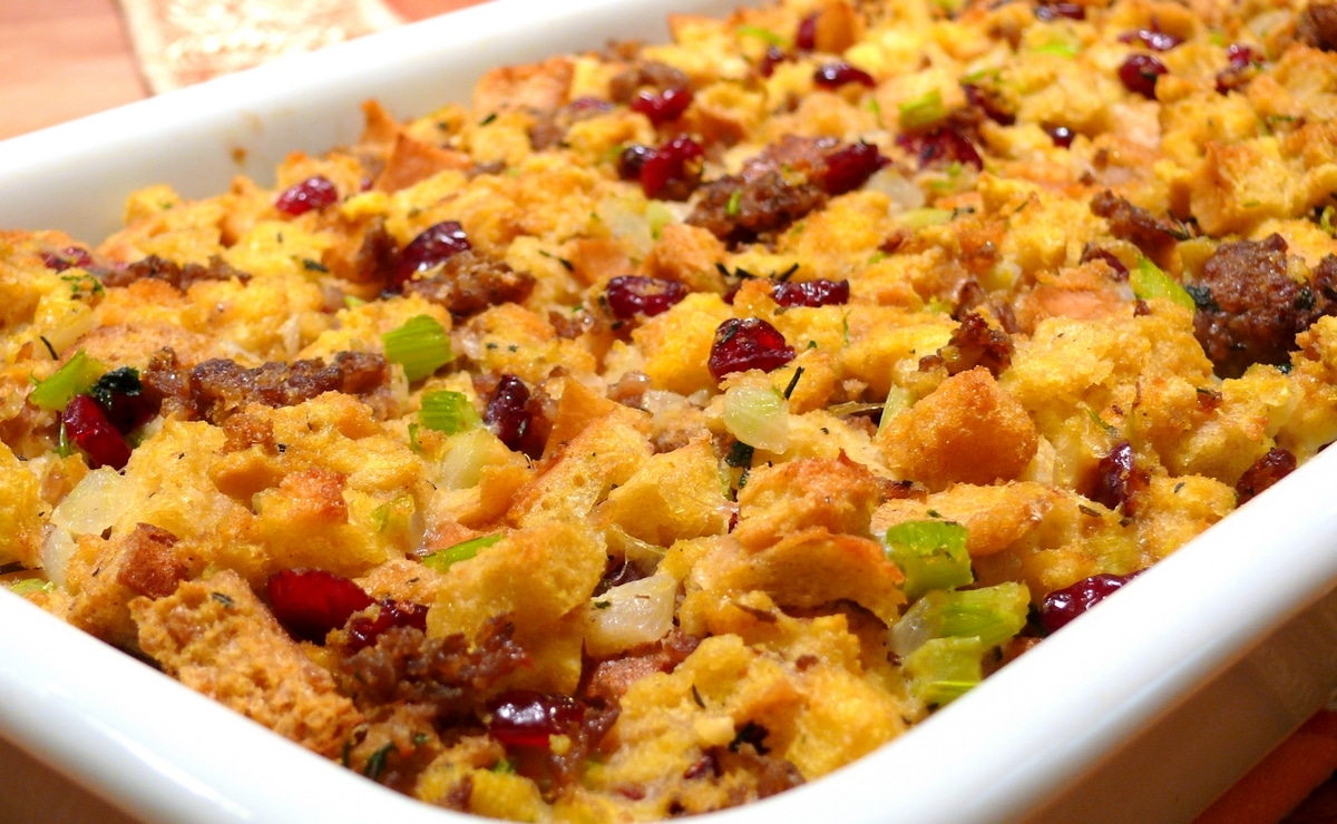 Side view of finished Bread and Sausage Stuffing with Cranberries Side view of bread and sausage stuffing with cranberries in a white baking dish, showcasing its golden-brown crust and hearty texture.