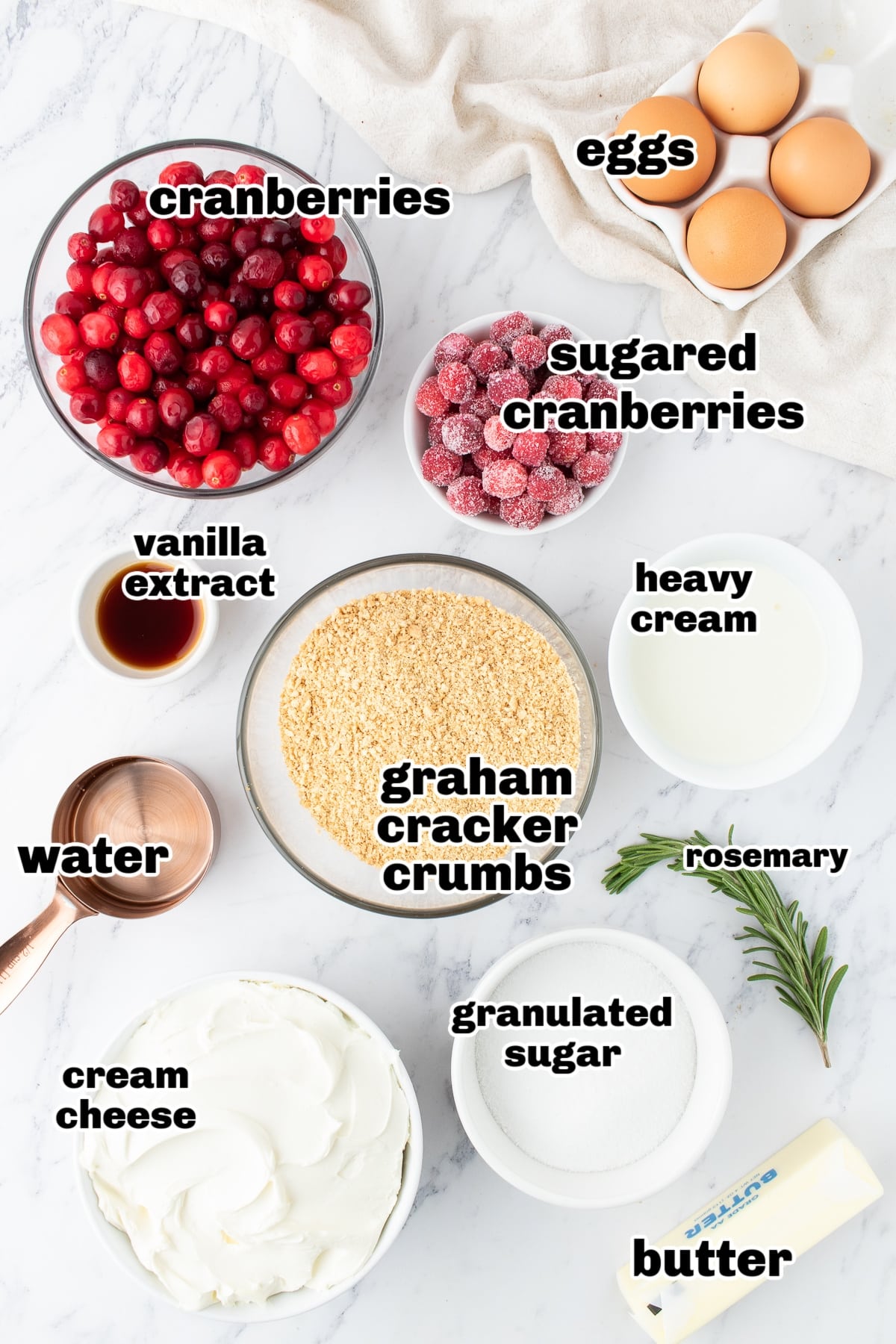 Ingredients for cranberry cheesecake arranged on a countertop, including cream cheese, cranberries, sugar, and graham crackers.