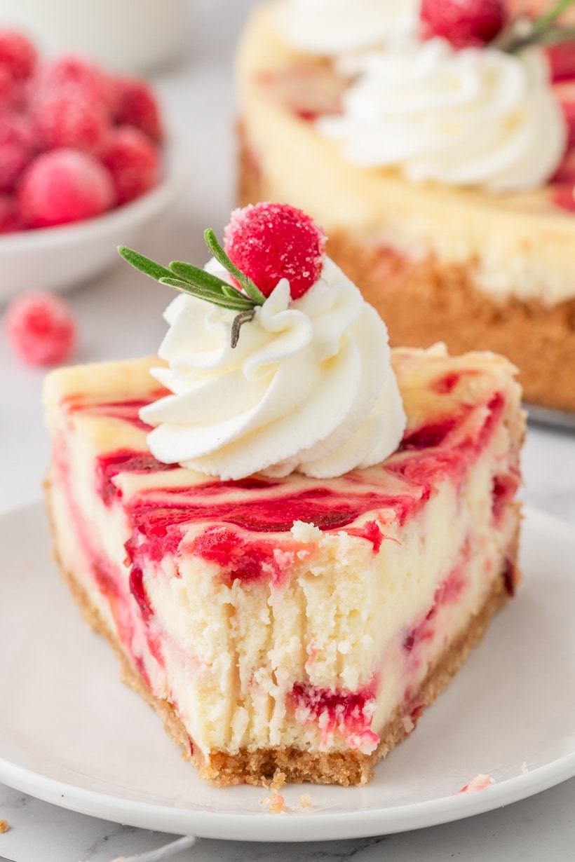A single slice of cranberry cheesecake on a plate with a fork and a bite taken, showing the creamy filling and cranberry swirl.