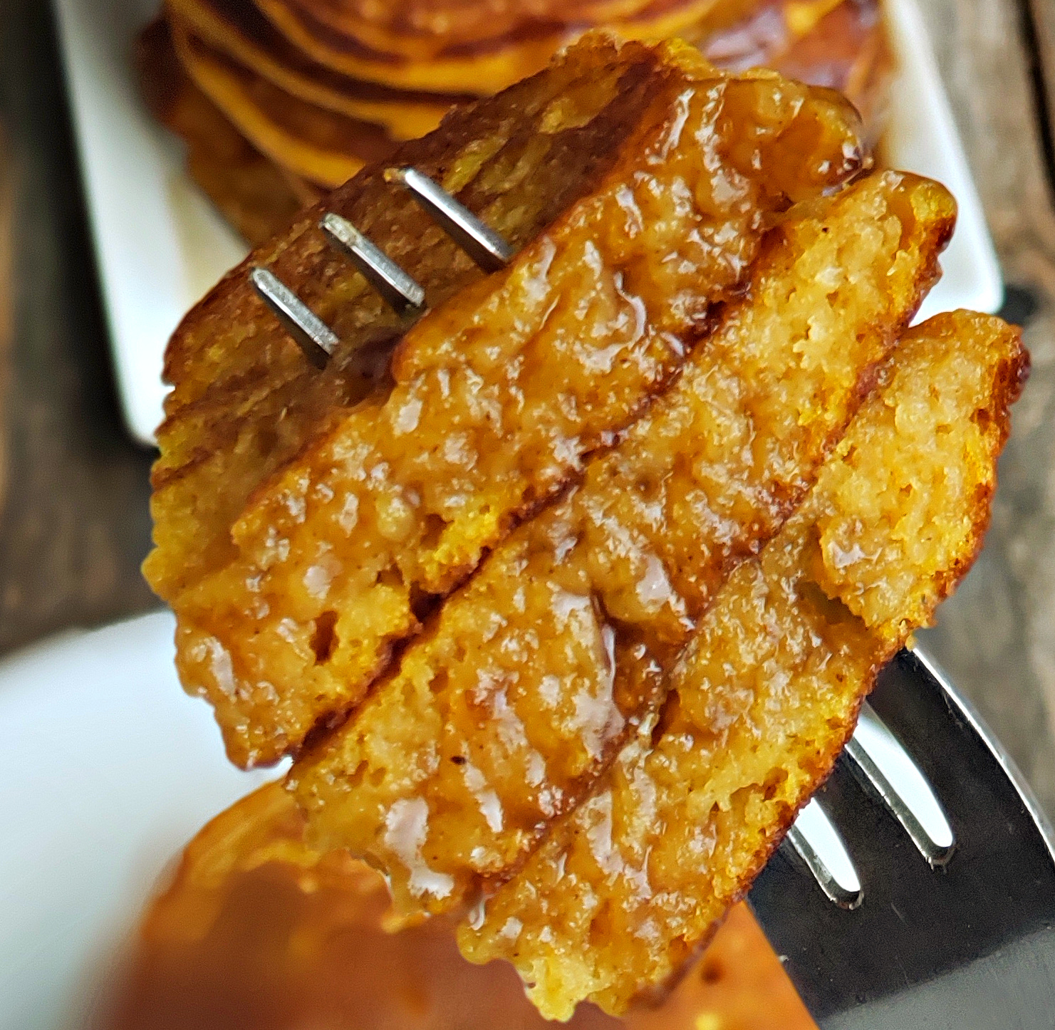 Fluffy pumpkin pancakes with cinnamon syrup bite. Close-up of fluffy pumpkin pancakes on a fork with cinnamon syrup soaking in.