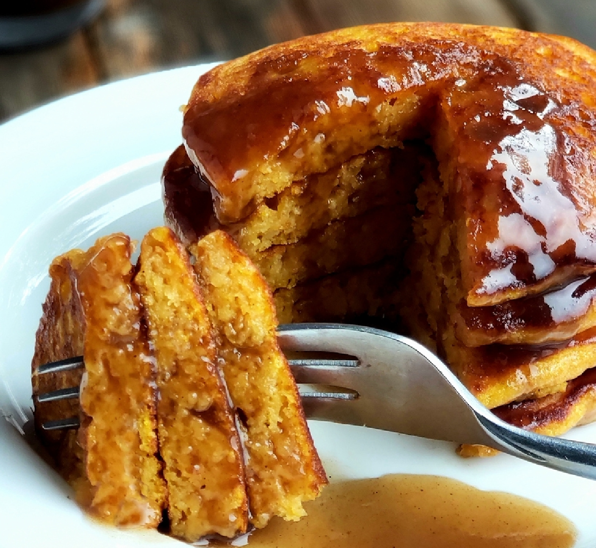 Pumpkin pancakes with cinnamon syrup served on a plate. Stack of pumpkin pancakes on a plate with a cut slice dripping in cinnamon syrup.