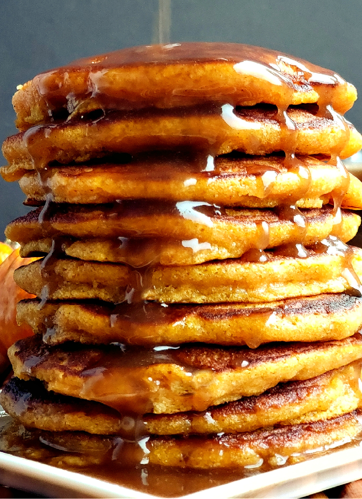 Fluffy pumpkin pancakes stacked with cinnamon syrup. Tall stack of fluffy pumpkin pancakes with cinnamon syrup poured over the top.